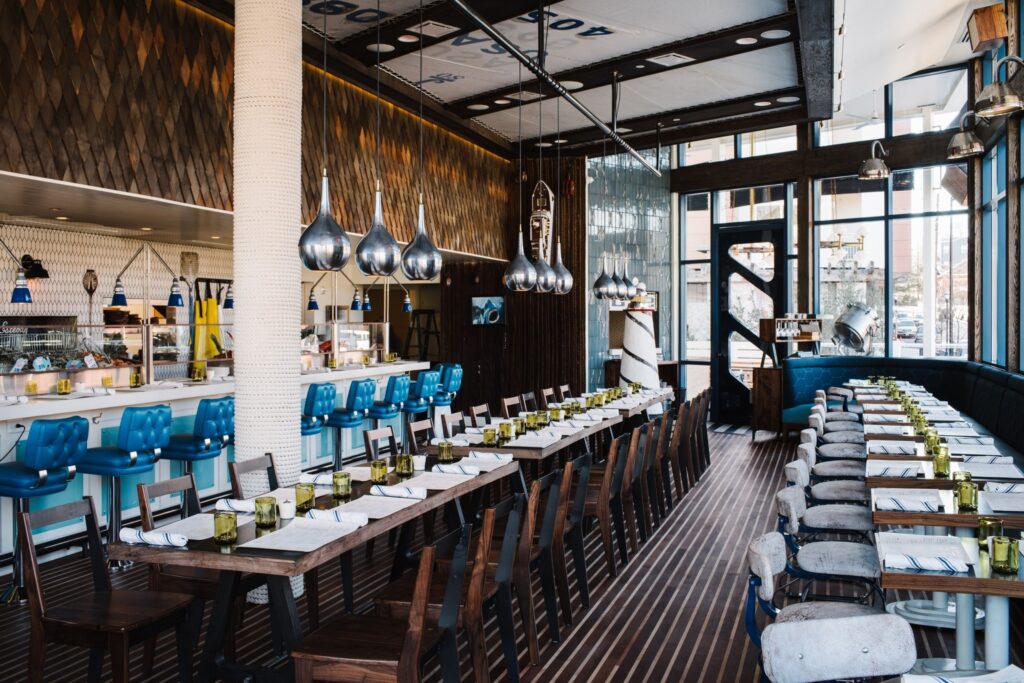 Blue stools at a white bar, long wooden table and chairs and a white pillar at BeetleCat
