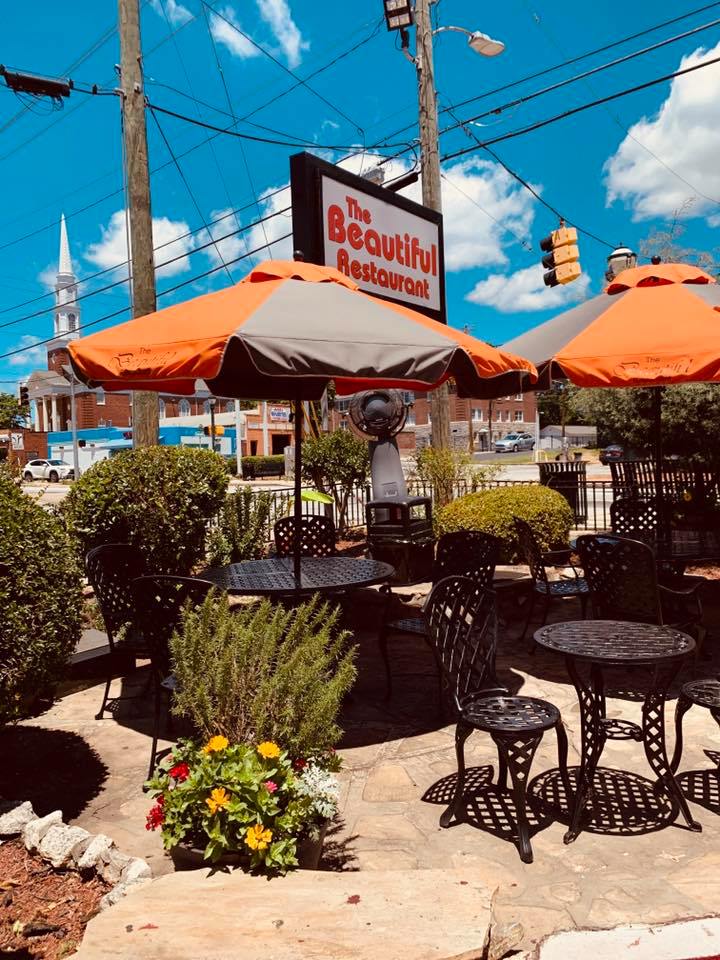 Orange umbrellas and Wrought iron chairs and tables arranged at a flower festooned patio at The Beautiful
