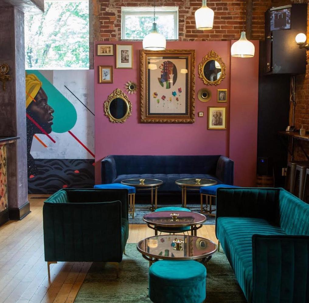 Colorful seating area furnished with emerald sofas; pink walls covered with mirrors, paintings and photographs at Parlor