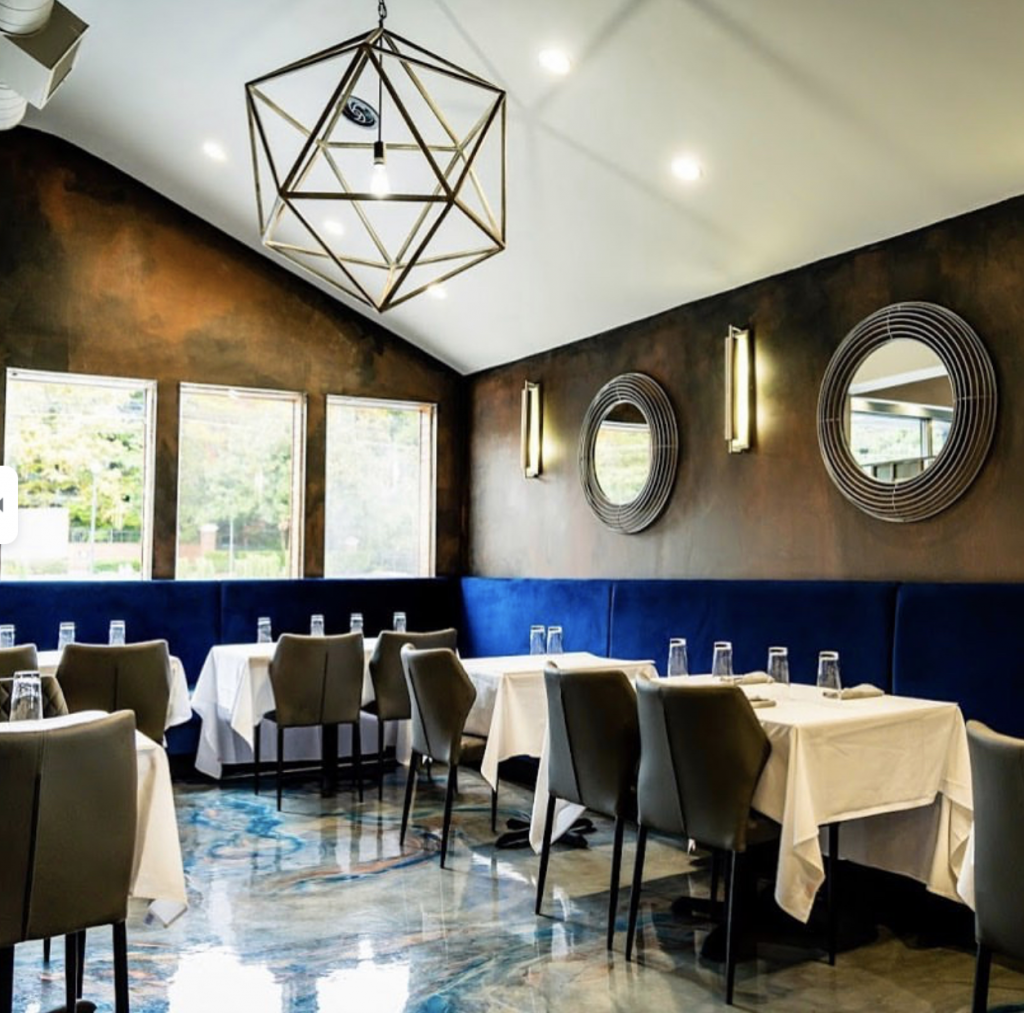 Restaurant interior with mirrors and light fixtures on brown walls, gray chairs and formally arranged tables and an ornate lamp hanging from the ceiling at Roc South