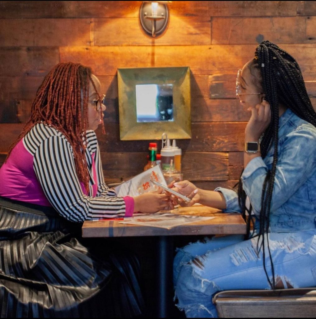 Two women seated and having a conversation at Tom, Dick, and Hank