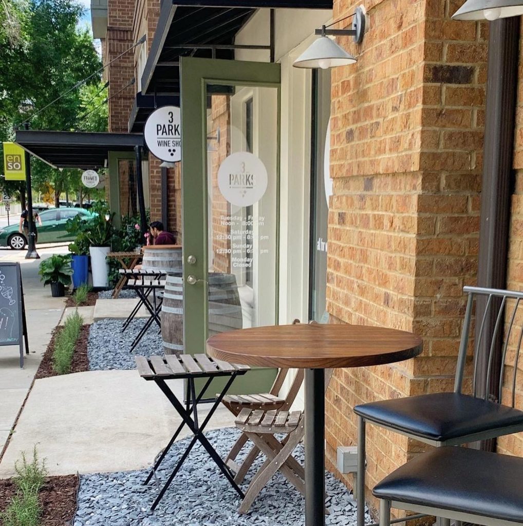 Chairs and tables arranged at the gravel covered entrance to a brick building at Three Parks Wine