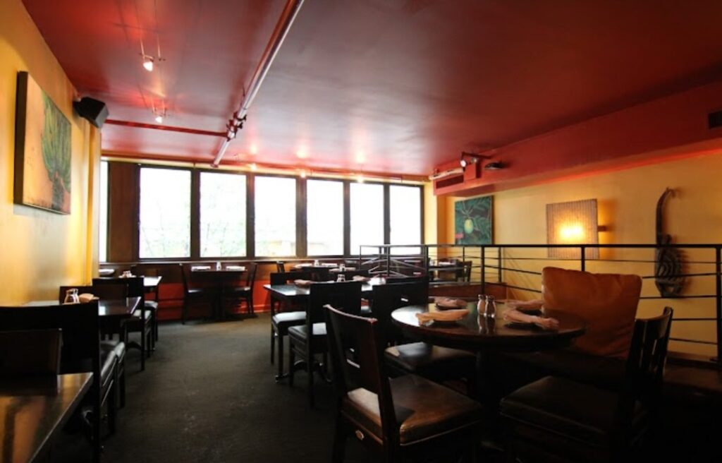 Interior of brightly painted restaurant furnished with dark, wooden chairs at Negril Village Nyc